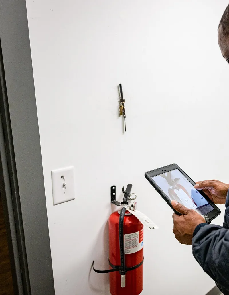 Wall-mounted fire extinguisher being inspected with a tablet