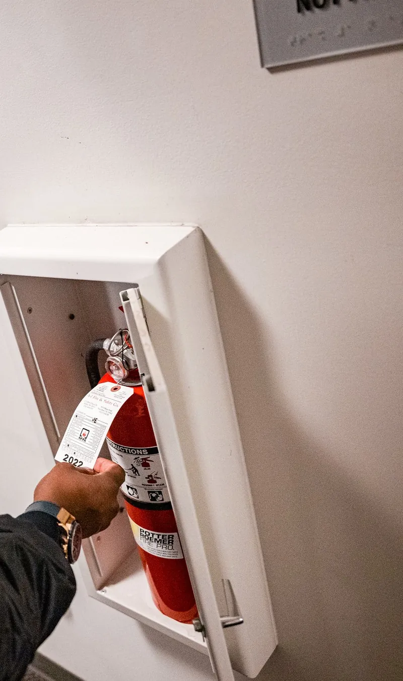 Fire extinguisher inspection tag being checked in a wall cabinet