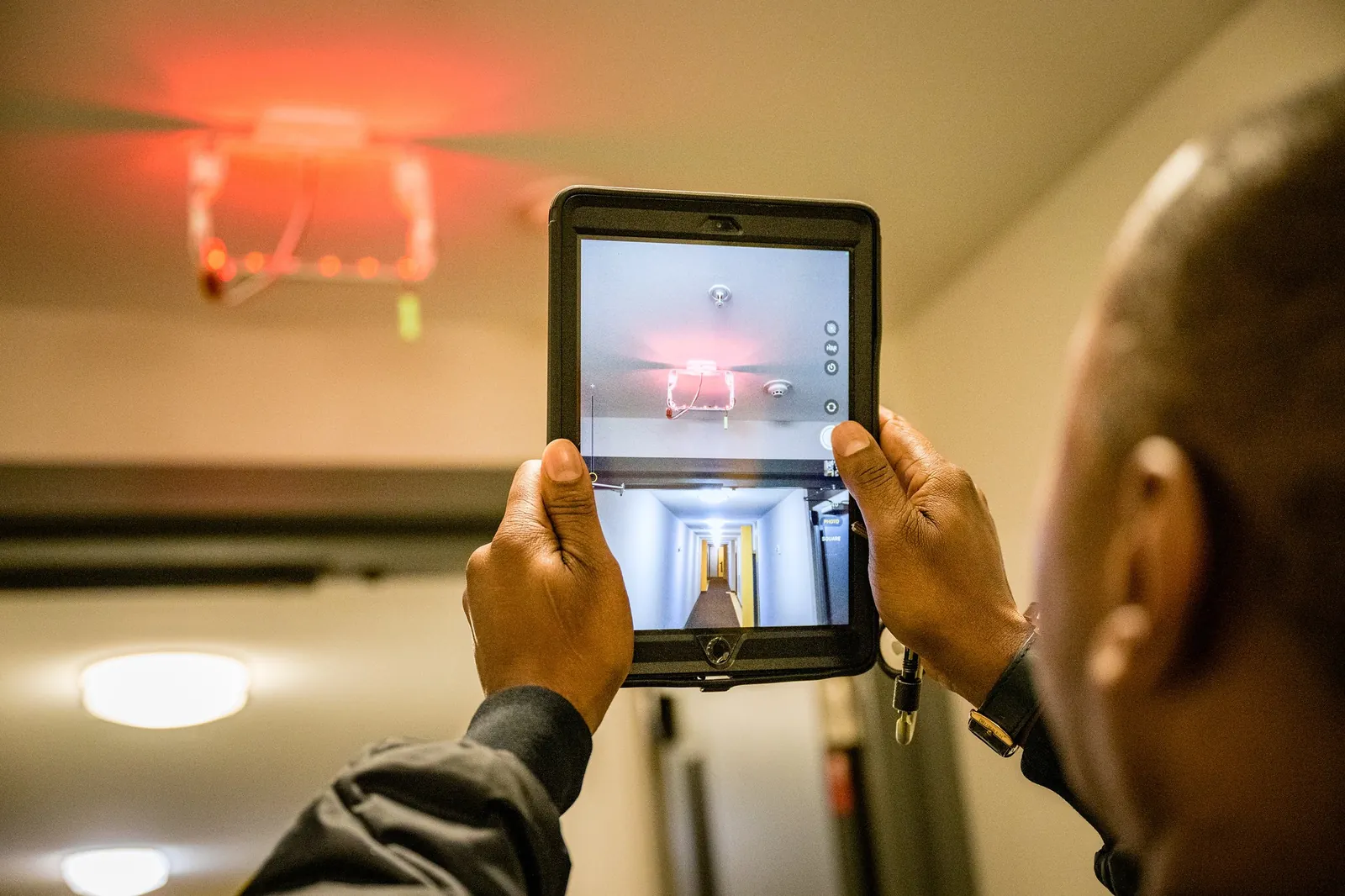 Inspector checking a ceiling fire alarm strobe with a tablet